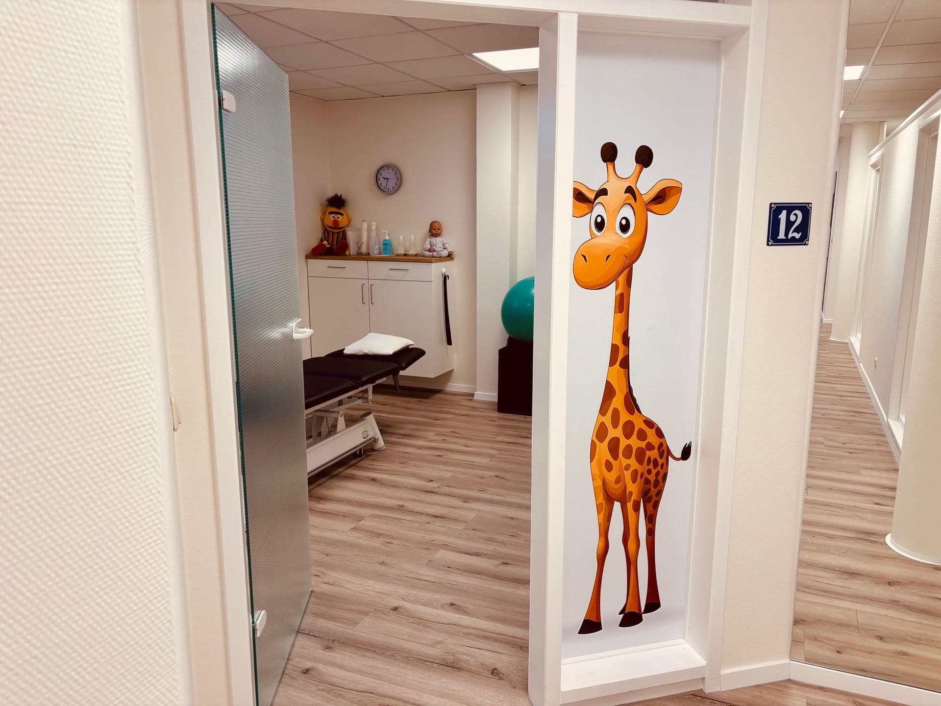 Kinderfreundlicher Behandlungsraum mit lustiger Giraffen-Wanddekoration in der KG Praxis Berkemeyer